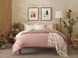 A cozy bedroom featuring a wooden bed dressed in Coyuchi’s Organic Crinkled Percale™ Sheet Set in soft pink and white, crafted from GOTS certified cotton, complemented by abstract wall art, a floor lamp, and plants in vases for a warm and inviting atmosphere with breathable bedding.