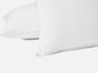 Two plain white Coyuchi Organic Crinkled Percale™ Shams overlap each other on a white background, their smooth, GOTS-certified cotton fabric showcasing clean edges and refined details that evoke the timeless quality of organic percale bedding.