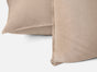 Two light brown Coyuchi Organic Crinkled Percale™ Shams are shown close up, made from breathable fabric with a softly crinkled percale texture—one laying flat and the other propped upright against it, both set against a plain white background.