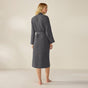 A person stands barefoot, facing away, wearing the Coyuchi Unisex Organic Waffle Robe in dark gray with a belt tied at the waist, set against a plain light background.