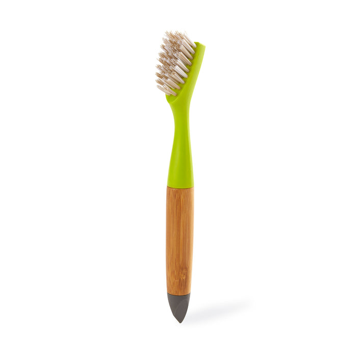 The Full Circle Micro Manager Detail Brush, featuring white bristles, a green plastic neck, a wooden handle, and a dark pointed tip, stands upright on a white background—ideal for precise kitchen cleaning.