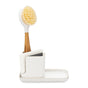 The Full Circle Ceramic Sinkside Caddy holds a dish brush with a wooden handle, a white sponge, and a scrub pad, all organized neatly on its tray to efficiently maximize your sink space.