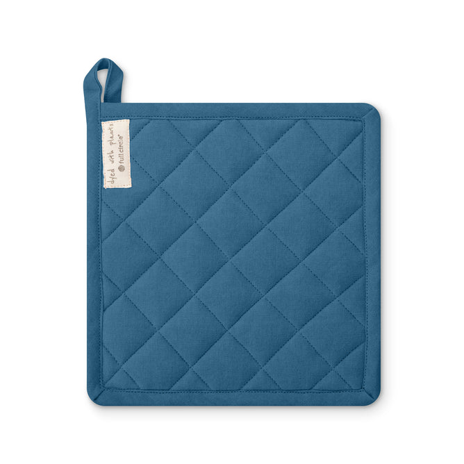 The Full Circle Kind Plant Dyed Trivet is a square, blue, organic cotton pot holder with diagonal stitching, a hanging loop, and a fabric tag. Naturally plant dyed, it’s shown on a white background.