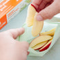 A person puts fresh apple slices into a green Full Circle Compostable Zipper Snack Bag, with the box labeled "Compostable Zipper Snack Bags" visible in the background.