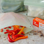 Sliced red and yellow bell peppers spill out of a reusable silicone bag on the counter, surrounded by sustainable storage options like freezer-safe bags and a Full Circle Compostable Zipper Gallon Bag box in the background.