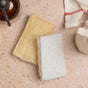 Two rectangular Full Circle 2pk Loofah Sponges—one natural loofah and one white plant-based cellulose—are displayed on a speckled countertop beside a towel, bottle, and container.