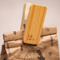 A sustainable kitchen essential, the Full Circle Bag Clip securely holds a folded brown paper bag adorned with black designs and text. The bamboo clip features an engraved Full Circle logo, with a blurred background.