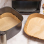 Two air fryer baskets lined with Full Circle FSC Certified Air Fryer Liners sit on a marble countertop, with the air fryer base visible in the background.