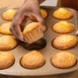 A hand lifts a freshly baked muffin from a tin lined with Full Circle FSC Certified Cupcake Liners, each muffin nestled in colorful, eco-friendly wrappers.