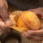 A person’s hands peel a FSC Certified Cupcake Liner by Full Circle off a golden muffin, with a muffin tin in the background.
