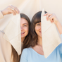 Two women smile while holding Fomin Clean Facial Towels Bamboo, each covering one eye, standing close together against a light background.