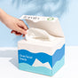 A hand pulls a white disposable face towel from an open Fomin Clean Facial Towels box, ideal for sensitive skin. The white box with blue accents is displayed on a white surface against a light blue background.