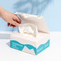 A hand pulls a white textured Fomin Exfoliating Facial Towel from an open white box with blue accents, labeled “Exfoliating Facial Towels,” resting on a white surface against a light blue background.