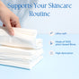 A hand lifts a Fomin Exfoliating Facial Towel from a stacked pile on blue. The ultra-soft towel is made of 100% plant-based fibers and offers high absorption.