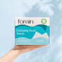 A hand holds a box of Fomin Exfoliating Facial Towels against a light blue background. The packaging highlights these plant-based, ultra-soft, disposable towels as tear-resistant and beneficial for clearer skin.