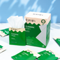 A box of Fomin Feminine Wipes sits on a light blue surface, one packet open to reveal a textured wipe. Green and beige packets for gentle cleansing and vaginal health from Fomin are scattered nearby.