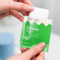 A person holds an open green and white Fomin Feminine Wipes packet, with a white wipe partially pulled out—gentle, sensitive wipes ideal for supporting vaginal health.