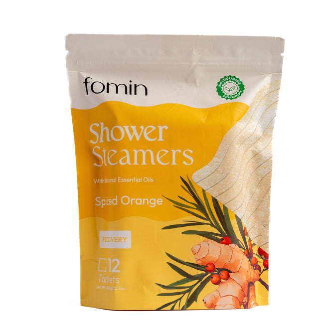 A yellow and white resealable pouch labeled Fomin Shower Steamer - Spiced Orange shows orange slices and ginger, emphasizes aromatherapy benefits, and contains 12 tablets with natural essential oils for recovery.