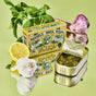 An open tin of Fishwife Mussels in Basil Pesto and its vibrant packaging rest on a glossy green surface, surrounded by basil, garlic, lemon, and red onion—ideal for mixing with pasta and olive oil.