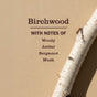 A birch branch rests against a beige wall. Text reads: Mrs. Meyer's Fabric Freshener Spray—Birchwood scent with woody, amber, bergamot, and musk notes for a long-lasting fragrance.