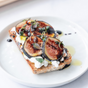 A slice of toast with cottage cheese, fresh figs, microgreens, and a drizzle of Kosterina Fig Balsamic Vinegar, served on a white plate.