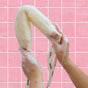 Two hands washing a Floofah 2-in-1 Exfoliating Back Scrubber, creating soap suds in front of a pink tiled wall.