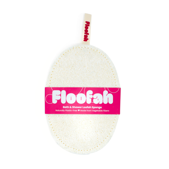 A white, oval-shaped Exfoliating Shower Loofah from Floofah features a beige hanging loop at the top and a pink label that highlights its plant-based, plastic-free composition made from natural luffa gourd fibers for sustainable cleaning.