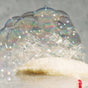 A close-up of iridescent soap bubbles forming on top of the white Floofah Exfoliating Shower Loofah, set against a gray background.