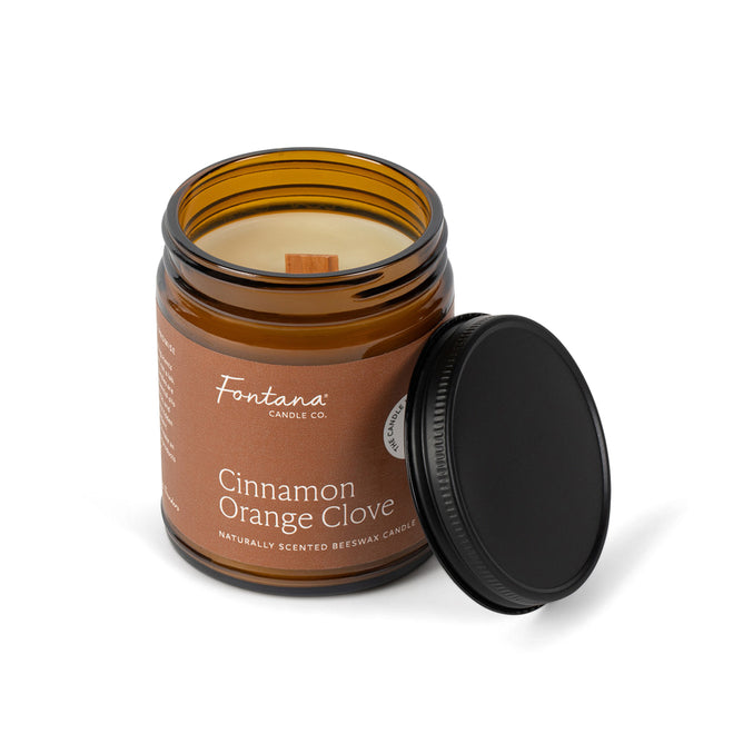 A brown glass jar candle labeled Cinnamon Orange Clove, with a black lid beside it, is made by Fontana Candle Co.; this natural scented candle features a wooden wick and is crafted from beeswax and coconut oil.