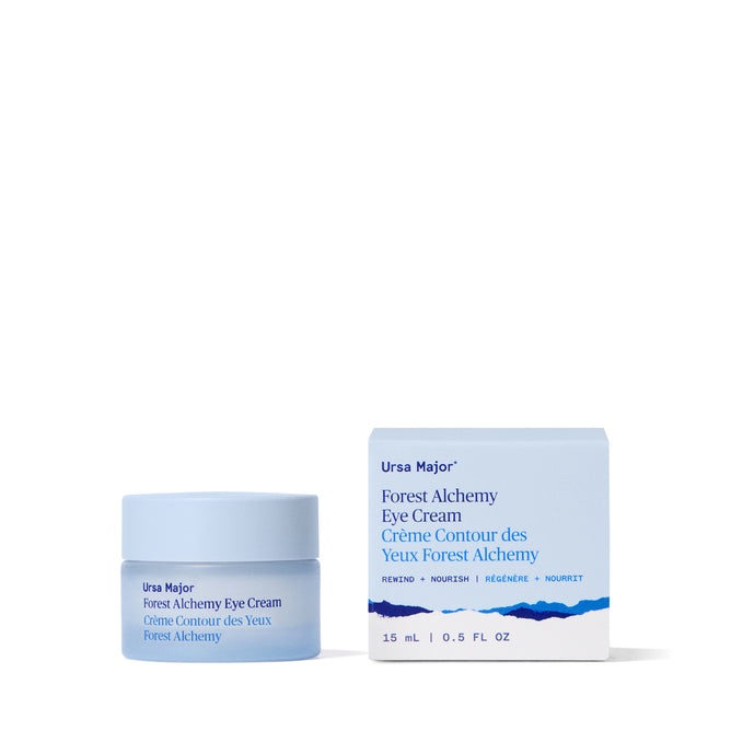 A light blue Ursa Major Forest Alchemy Eye Cream jar and matching box with blue text describing its benefits for fine lines and dark circles, shown on a white background.