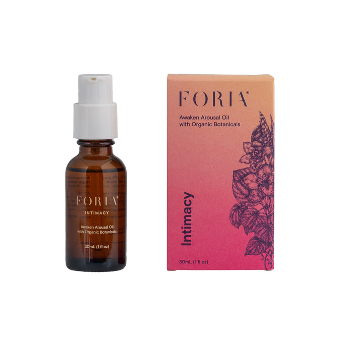 A brown glass pump bottle labeled “Foria Intimacy Awaken Arousal Oil with Organic Botanicals” stands by a pink-orange floral box, highlighting this Foria blend with natural botanicals for enhanced intimate pleasure.