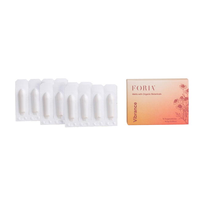 Eight white suppositories in plastic packaging are arranged next to a rectangular Foria Vibrance Melts with Organic Botanicals box, featuring an orange gradient and floral design, emphasizing these hydrating melts for internal hydration.