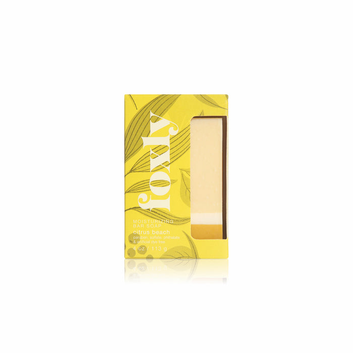 A yellow 113g Foxly Moisturizing Bar Soap box in Citrus Beach scent displays a botanical leaf pattern and clear window revealing its light yellow soap. Handcrafted with nourishing oils for a creamy lather.
