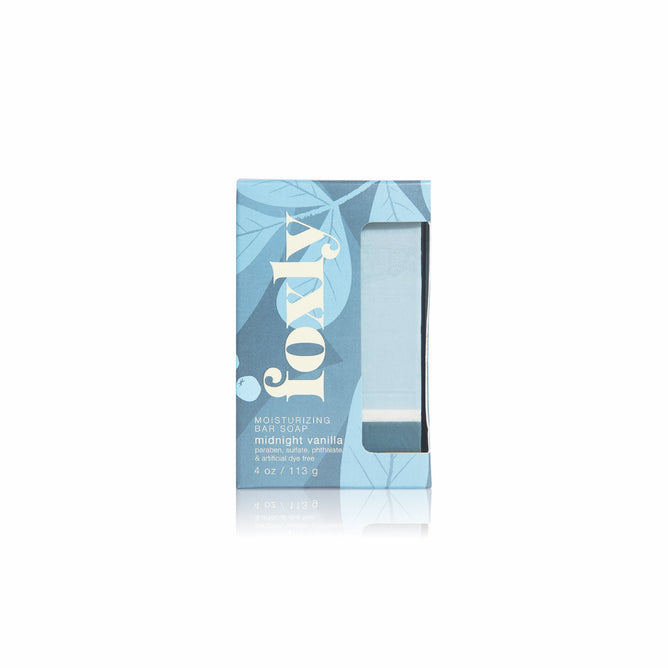 A rectangular box of Foxly Moisturizing Bar Soap in Midnight Vanilla, with a blue leaf pattern and clear window showcasing the clean-ingredient soap, is reflected on a white surface.