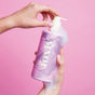 A person pumps foamy Foxly Body Wash with nourishing oils from a pink and purple bottle labeled Foxly against a matching pink background.