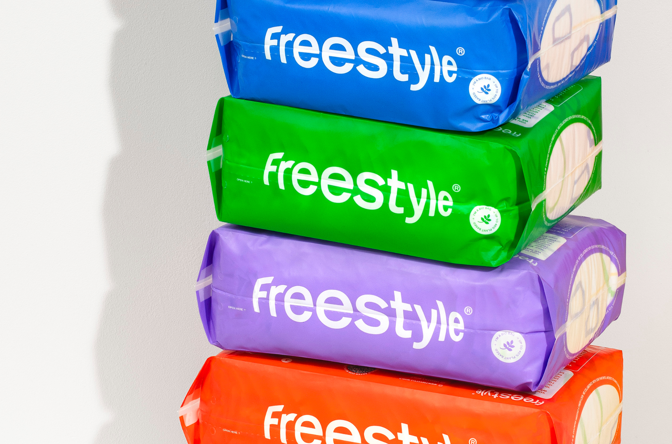 Four packages of “freestyle” diapers stacked vertically. The packages are blue, green, purple, and orange, each featuring the brand name in white lettering and a small leaf logo.