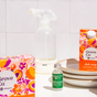 The Grove Co. Multi-Purpose Cleaner Starter Set - Summer Collection is displayed on a white surface next to stacked plates, featuring branded bottles and packaging against a white tiled background.