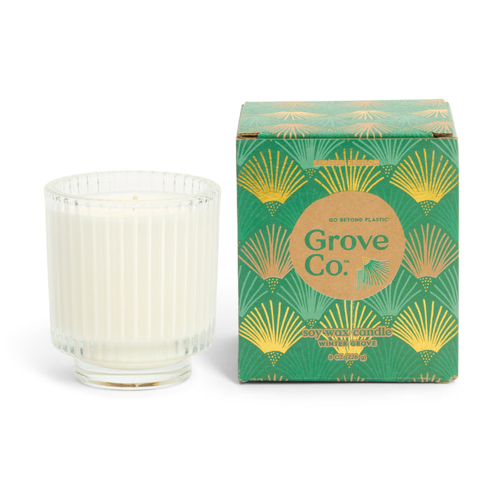 A white soy wax blend candle in a ribbed glass jar stands beside a green and gold Grove Co. box with an art deco leaf design, labeled "Soy Wax Blend Candle – Winter Collection" and featuring a natural origin fragrance.