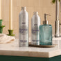 Two silver patterned bottles labeled “Grove Co. Hand Soap Refill - Winter Collection” stand on a countertop next to a blue ribbed glass soap dispenser on a silver tray.