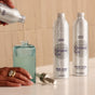 A hand pours Grove Co.'s Hand Soap Refill - Winter Collection from a silver bottle into a blue glass dispenser, while two Grove Co. refill bottles labeled dish and hand soap with natural fragrances sit on the countertop nearby.