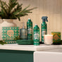 Grove Co. Hand Soap Refill - Winter Collection is displayed on a counter by a sink, with green plates, a glass soap dispenser, and pine branches in the background, creating a warm and inviting atmosphere.