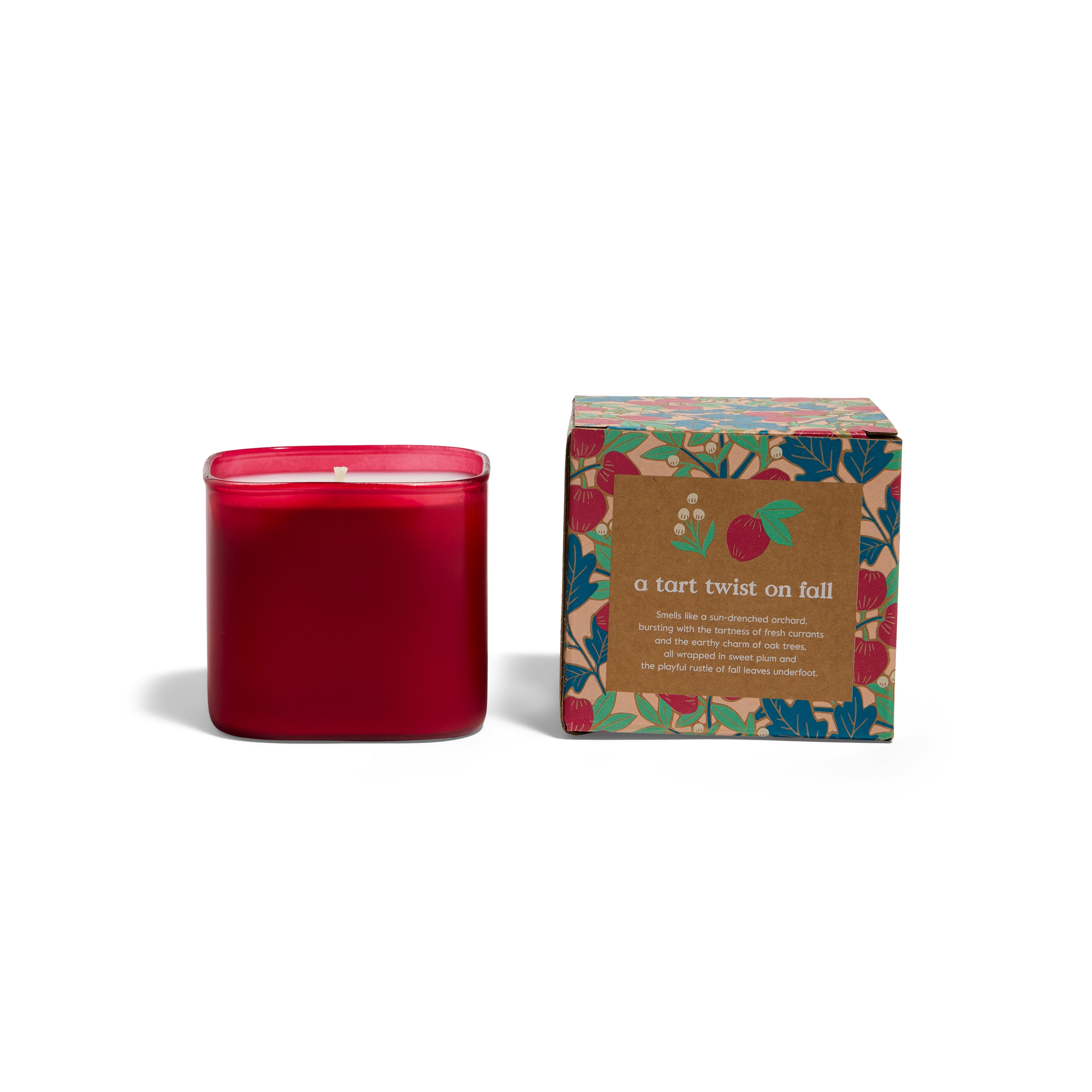A red, square glass Grove Co. Candles 9.5oz - Fall Collection sits beside its box with colorful leaves and a brown label. The autumn-inspired, eco-friendly design reads “a tart twist on fall.”.