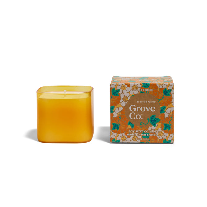 A yellow, square soy wax Candle - Fall Collection by Grove Co. sits by a decorative box with a white floral and leaf design, offering an eco-friendly touch perfect for the cozy season.