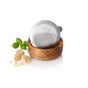 The AdHoc Cut'N Serve Fine Round Grater, featuring a sharp stainless steel blade, rests on an acacia wood bowl with fresh basil leaves and Parmesan chunks arranged nearby on a white background.