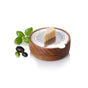 The AdHoc Cut'N Serve Fine Round Grater features a wooden base and stainless steel top for precise Parmesan grating. Fresh basil leaves and green and black olives accent it on a clean white background.