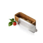 The AdHoc Cut'N Serve Fine Rectangle Grater, paired with its wooden acacia bowl and filled with grated cheese, is displayed beside a fresh basil sprig and a red cherry tomato on a white background.