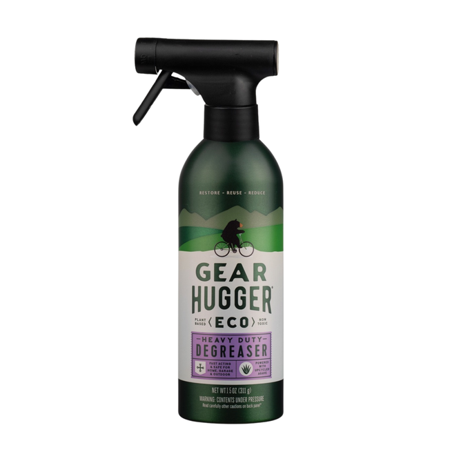A dark green spray bottle labeled Gear Hugger Heavy Duty Degreaser, adorned with eco-friendly symbols and a cyclist graphic over a green landscape. This plant-based formula from Gear Hugger delivers powerful heavy-duty cleaning using non-toxic ingredients for an environmentally responsible clean.