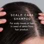 Close-up of a person parting dark hair reveals their scalp. Overlaid text: Good Juju Body & Home Scalp Care Conditioner Bar—for dandruff relief or detoxing product build-up—use with our Scalp Care Shampoo for best results.