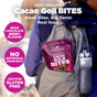A person outdoors with a gray backpack holds a pouch of Navitas Organics Superfood+ Cacao Goji BITES—gluten-free snacks with rich chocolate berry flavor and no artificial ingredients.