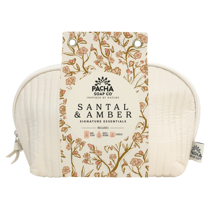 The Self Care Spa Set - Santal & Amber by Pacha Soap Co. includes soap, body wash, bath bomb, and candle in a cream-colored quilted pouch with a floral tag. Enjoy a woodsy scent for the perfect self-care gift set.
